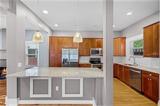 kitchen featuring light wood-style flooring, a sink, a kitchen island, stainless steel appliances, and light stone countertops