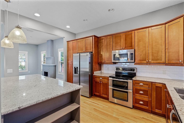 kitchen with brown cabinetry, light wood-style flooring, light stone countertops, and stainless steel appliances