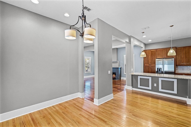 kitchen featuring visible vents, stainless steel refrigerator with ice dispenser, backsplash, brown cabinetry, and light wood finished floors