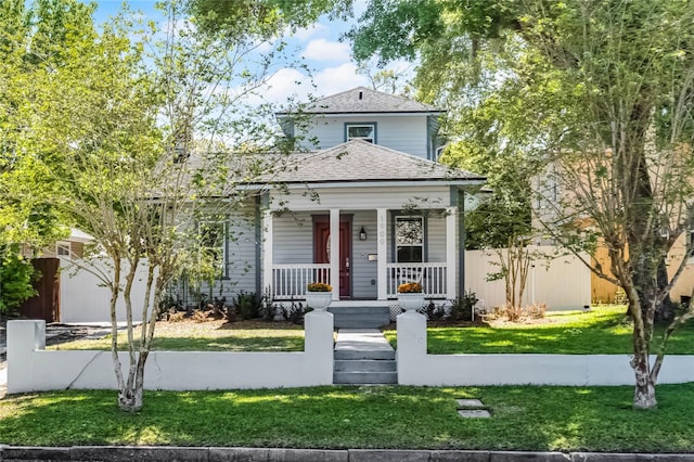 view of front of property featuring a porch, roof with shingles, a front lawn, and fence