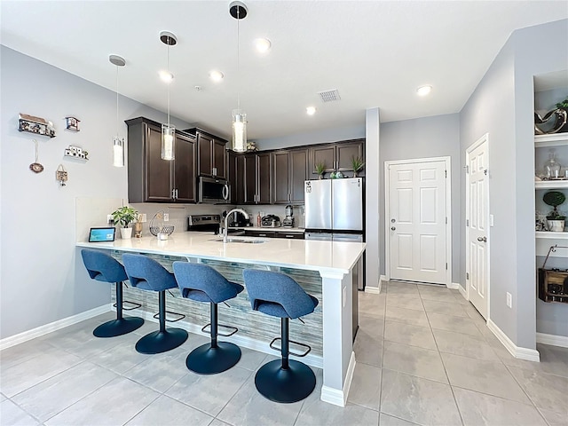 kitchen with a peninsula, dark brown cabinetry, stainless steel appliances, and a kitchen breakfast bar