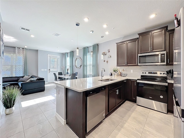 kitchen with dark brown cabinetry, visible vents, open floor plan, stainless steel appliances, and a sink