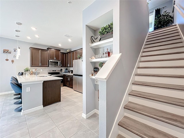 kitchen featuring open shelves, stainless steel appliances, dark brown cabinetry, a sink, and a peninsula