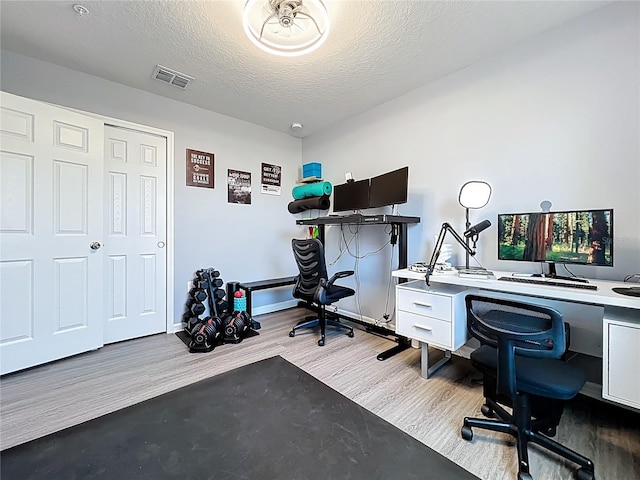 office with baseboards, a textured ceiling, visible vents, and wood finished floors