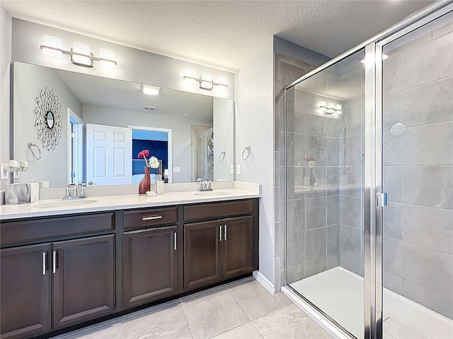 full bath with double vanity, a stall shower, a textured ceiling, and a sink