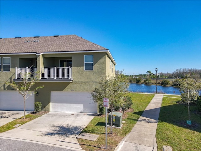 view of front facade with concrete driveway, a balcony, stucco siding, a water view, and a front yard