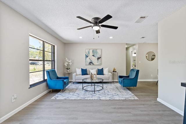 living area with a textured ceiling, recessed lighting, wood finished floors, visible vents, and baseboards