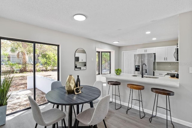 dining area with a textured ceiling, light wood finished floors, plenty of natural light, and baseboards