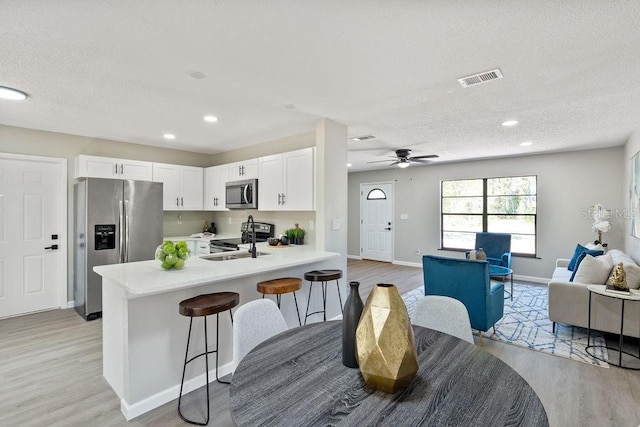 kitchen featuring visible vents, open floor plan, a peninsula, stainless steel appliances, and light countertops