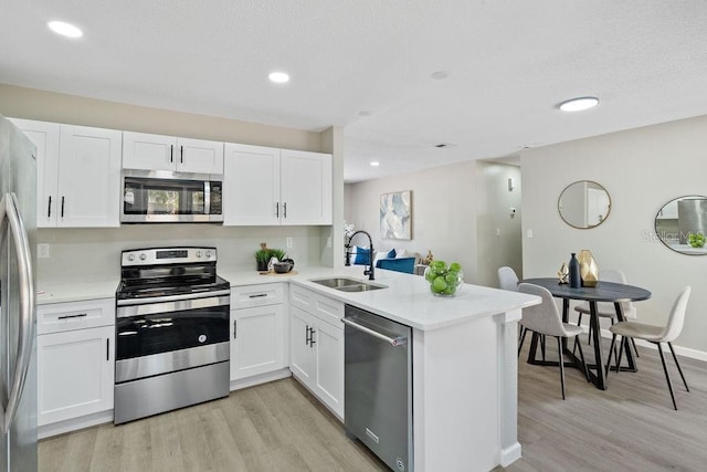 kitchen with stainless steel appliances, light wood-type flooring, a peninsula, and a sink