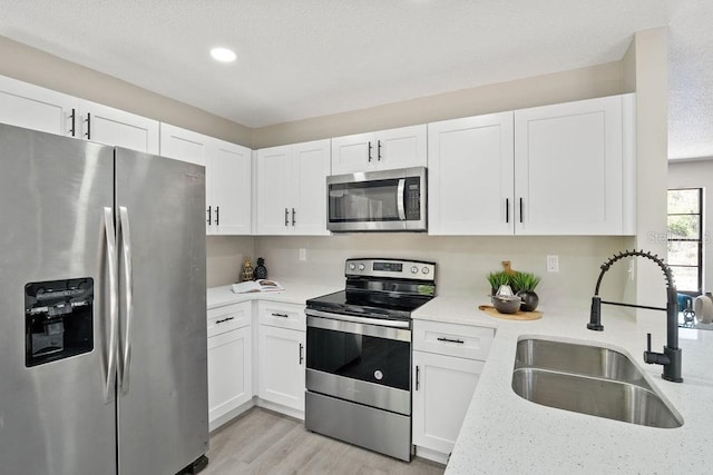 kitchen with light wood-style flooring, white cabinetry, stainless steel appliances, and a sink