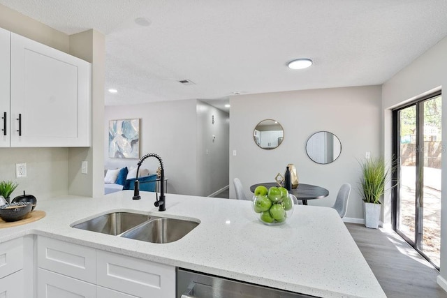 kitchen with a peninsula, a sink, visible vents, white cabinets, and light stone countertops