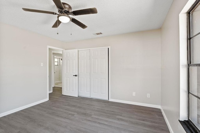 unfurnished bedroom featuring baseboards, a textured ceiling, visible vents, and wood finished floors