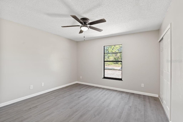 unfurnished bedroom with a textured ceiling, ceiling fan, wood finished floors, baseboards, and a closet