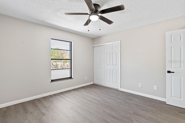 unfurnished bedroom with baseboards, a ceiling fan, wood finished floors, a textured ceiling, and a closet