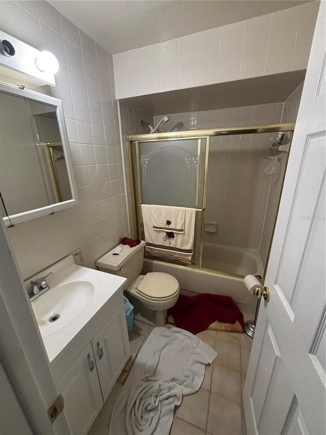 bathroom with tile patterned flooring, toilet, bath / shower combo with glass door, vanity, and tile walls