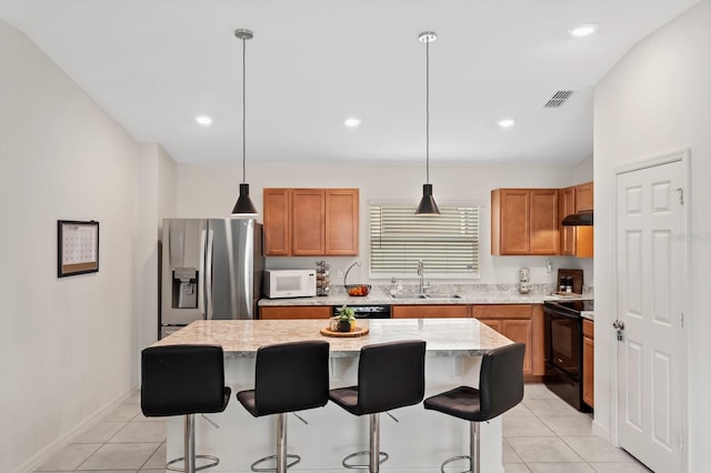 kitchen with a breakfast bar area, under cabinet range hood, a kitchen island, a sink, and black appliances