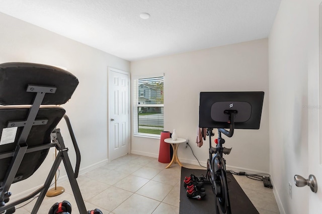 workout area featuring light tile patterned flooring, a textured ceiling, and baseboards