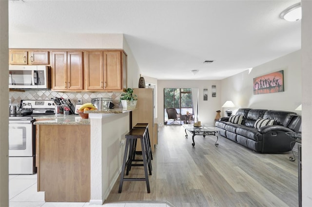 kitchen featuring tasteful backsplash, visible vents, open floor plan, a breakfast bar, and stainless steel appliances