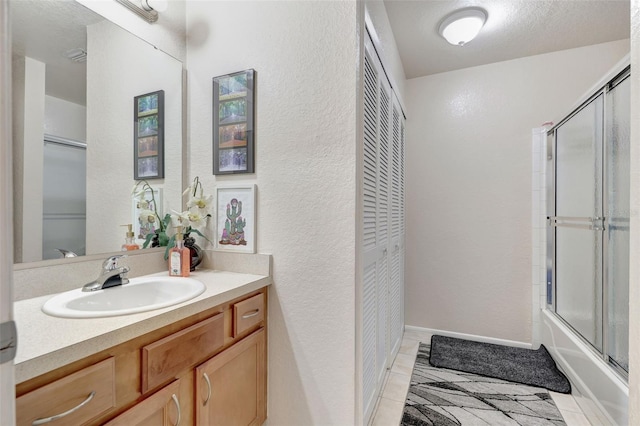 bathroom with vanity, baseboards, bath / shower combo with glass door, a closet, and a textured wall