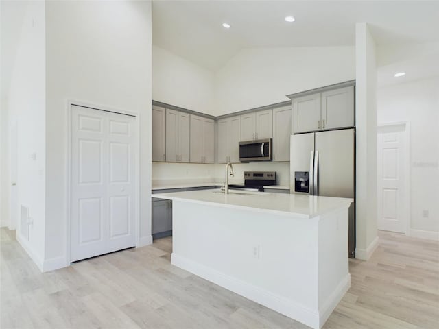 kitchen with a center island with sink, light countertops, gray cabinets, stainless steel appliances, and a sink