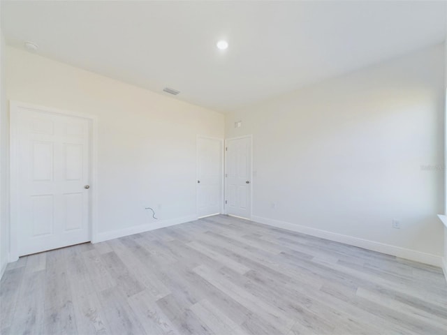 spare room featuring light wood-type flooring, visible vents, and baseboards