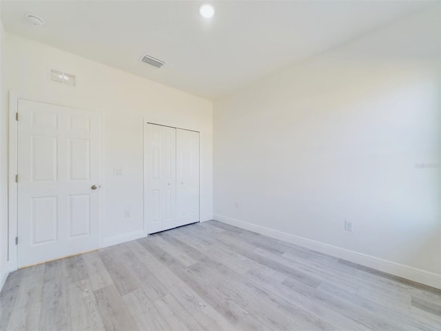 unfurnished bedroom with light wood-style flooring, visible vents, baseboards, and a closet