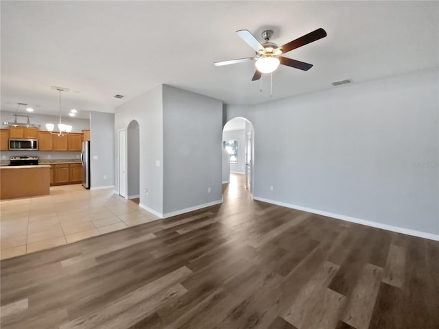 unfurnished living room with arched walkways, baseboards, visible vents, and light wood-style floors