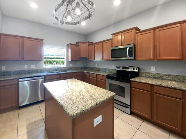 kitchen with light tile patterned floors, stone countertops, a sink, appliances with stainless steel finishes, and a center island