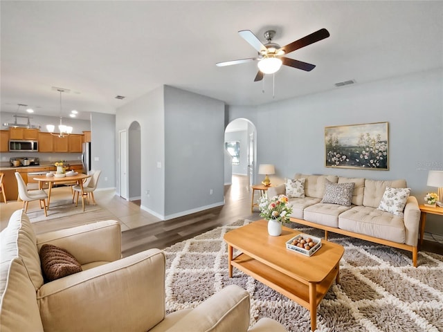 living room featuring visible vents, arched walkways, baseboards, light wood-style floors, and ceiling fan with notable chandelier