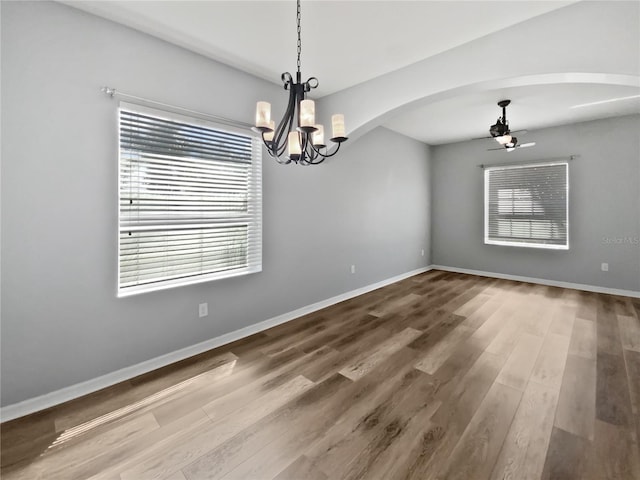 unfurnished dining area with ceiling fan with notable chandelier, wood finished floors, and baseboards