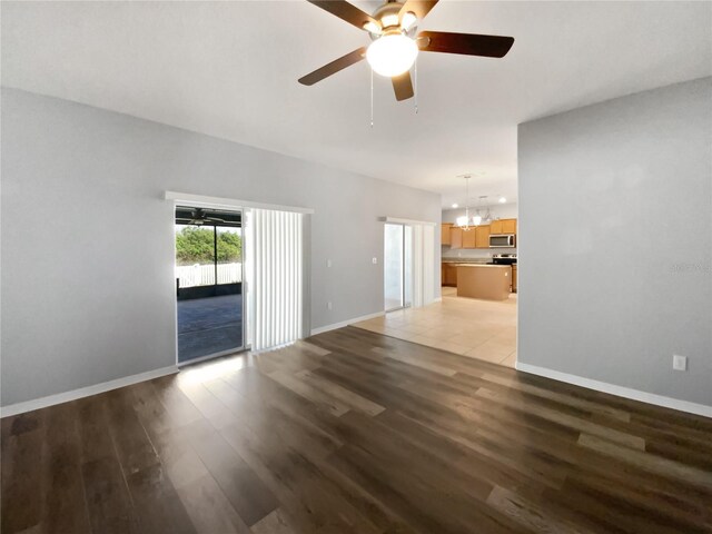 unfurnished living room featuring ceiling fan with notable chandelier, light wood finished floors, and baseboards