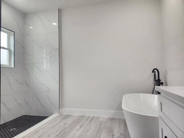 bathroom featuring a marble finish shower, baseboards, wood finished floors, vanity, and a freestanding tub