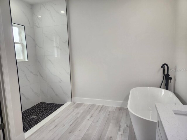 full bathroom with a freestanding bath, wood finished floors, a marble finish shower, and baseboards