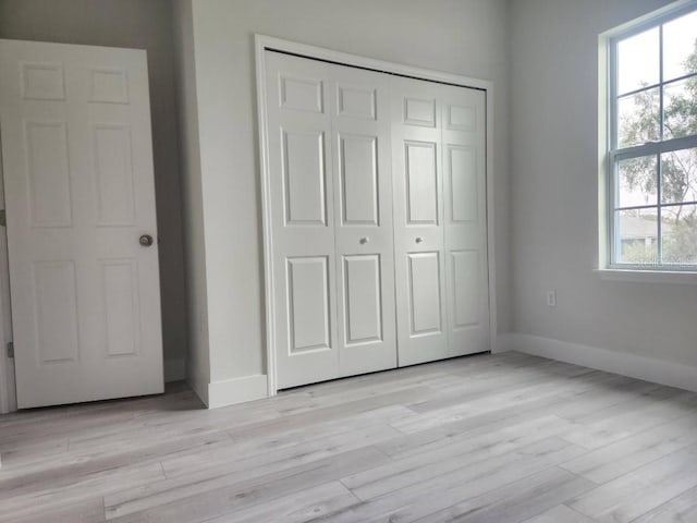 unfurnished bedroom featuring light wood finished floors, a closet, and baseboards