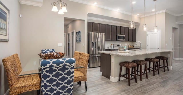 kitchen featuring a breakfast bar area, ornamental molding, stainless steel appliances, light wood-style floors, and a sink