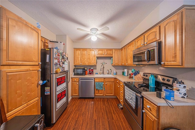 kitchen with a sink, a ceiling fan, light countertops, appliances with stainless steel finishes, and dark wood finished floors