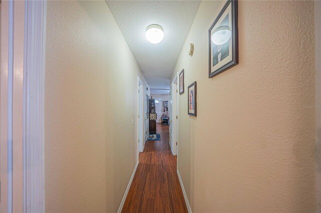 hallway featuring dark wood-style floors, baseboards, a textured ceiling, and a textured wall