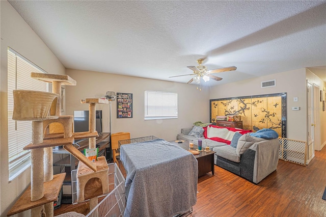 living area featuring a ceiling fan, a textured ceiling, visible vents, and wood finished floors