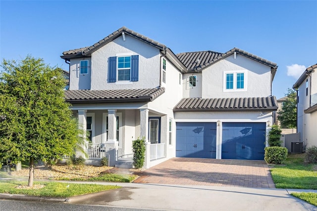 mediterranean / spanish home featuring decorative driveway, a tile roof, stucco siding, covered porch, and a garage