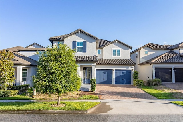 mediterranean / spanish house with a garage, decorative driveway, a tile roof, and stucco siding