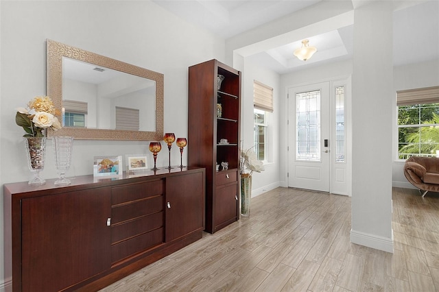 foyer entrance with light wood finished floors, a raised ceiling, and baseboards