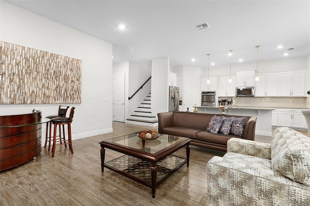 living area with baseboards, visible vents, stairway, and light wood finished floors