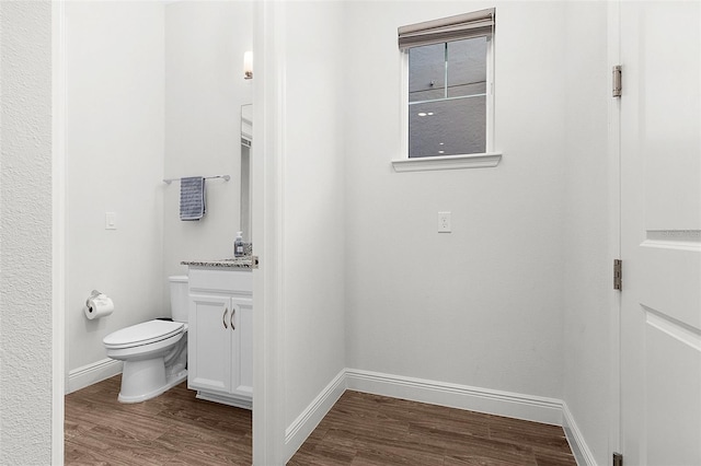 half bath with toilet, wood finished floors, vanity, and baseboards