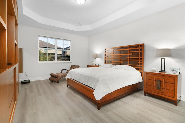 bedroom with a tray ceiling, light wood-style flooring, and baseboards