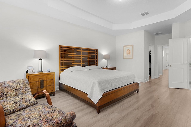 bedroom with light wood-style flooring, visible vents, a tray ceiling, and baseboards