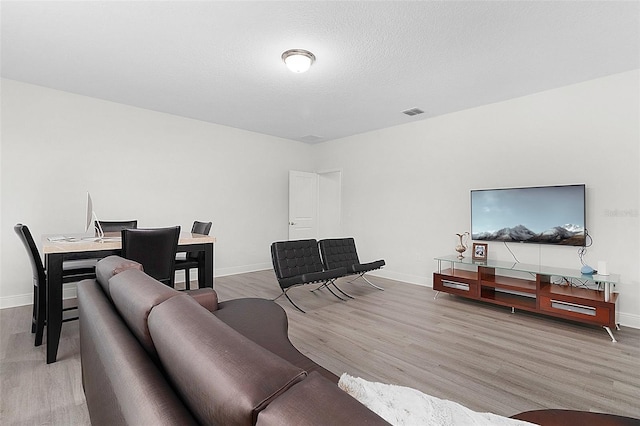 living room with baseboards, a textured ceiling, visible vents, and light wood-style floors