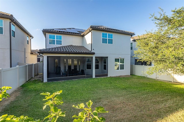 rear view of house featuring a yard, a sunroom, roof mounted solar panels, a fenced backyard, and a tiled roof