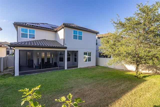 rear view of property with a sunroom, a fenced backyard, a lawn, and roof mounted solar panels