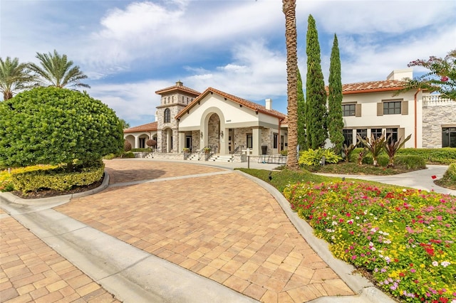 mediterranean / spanish-style home featuring stone siding, a tile roof, a chimney, and stucco siding